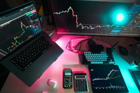 Trading setup with laptop, monitor, smartphone, and tablet displaying financial charts and data on a desk.