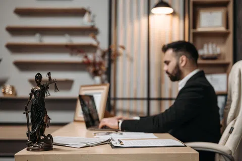 Lawyer working on laptop at desk with legal books and Lady Justice statue in modern office setting