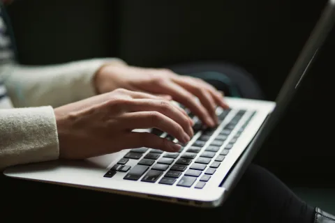 Close-up of hands typing on a laptop keyboard in a dimly lit environment
