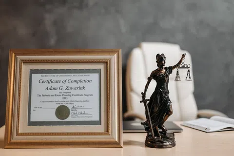 Framed Certificate of Completion for Adam G. Zuiwerink and a bronze Lady Justice statue on a wooden desk.