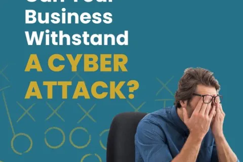 Man in glasses at desk covering face, text asks if your business can withstand a cyber attack on blue background.