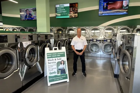 Man standing in modern laundromat with rows of washers and a wash and fold service sign