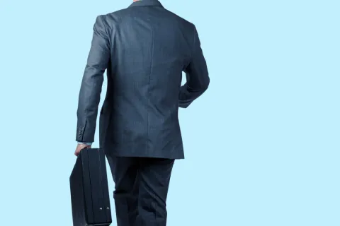 Businessman in dark suit walking away holding a briefcase against a light blue background