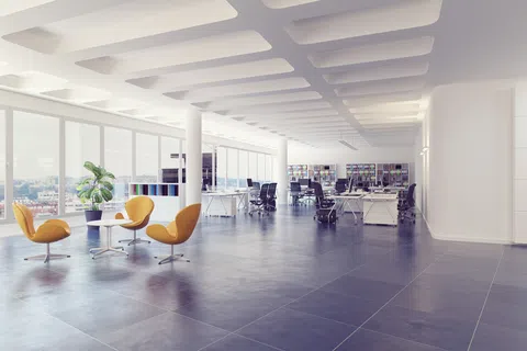 Modern open-plan office with large windows, yellow chairs, desks, black office chairs, and bookshelves.