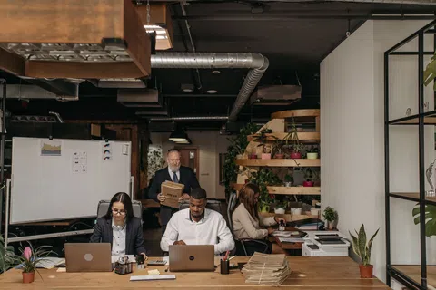 Diverse team working on laptops in modern office with plants and documents on wooden desk and shelves