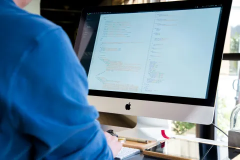 Person coding on an Apple iMac computer displaying programming code on highlighting the usefulness of local IT.