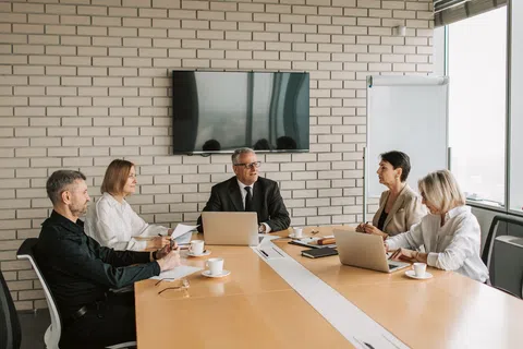 Business team of five in formal attire having a meeting in a modern office conference room.