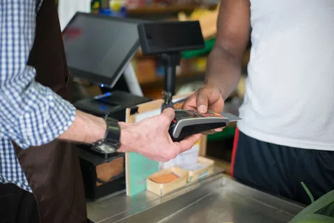 Customer making contactless payment with card at store checkout counter held by cashier