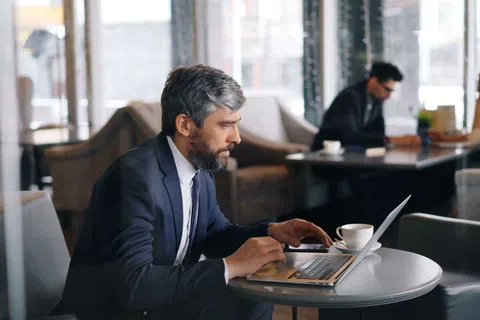 Man in suit working on laptop at cafe table with coffee cup, focused and professional environment.