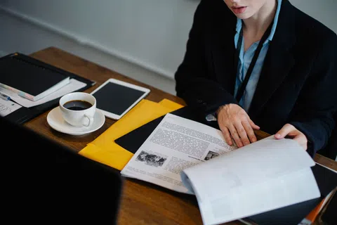 Person in business attire reading documents at desk with coffee, tablet, and folders.