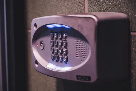 Close-up of a metal keypad entry system with illuminated blue light on a textured wall at night.
