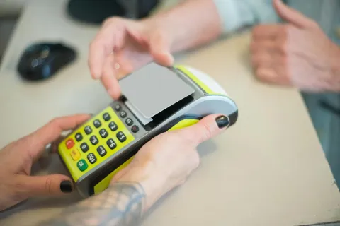 Person making contactless payment using a card and handheld POS terminal at a counter.