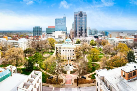 Aerial view of a city park with historic buildings, tall skyscrapers, and autumn trees under a blue sky.