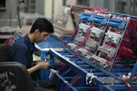 Technician assembling and wiring electrical control panels with organized cables in an industrial setting.