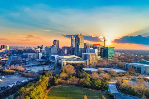 Sunset over a city skyline with tall buildings, green park in foreground, and a vibrant sky with clouds.