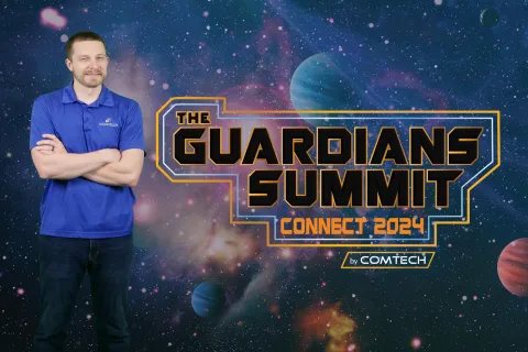 Man in blue polo stands with arms crossed beside The Guardians Summit Connect 2024 by Comtech logo over galaxy background.