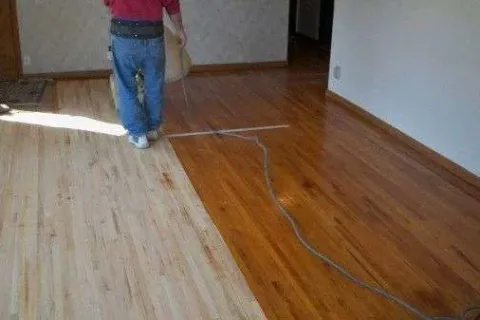 Person refinishing a hardwood floor showing contrast between sanded light wood and finished darker wood.