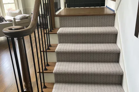 Indoor wooden staircase with patterned carpet runner and black metal balusters in a bright living room.
