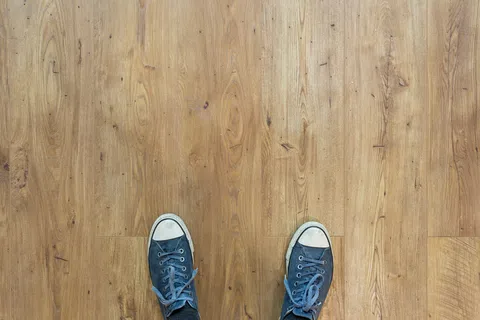 Top view of worn blue sneakers on a wooden floor with natural grain patterns and knots.