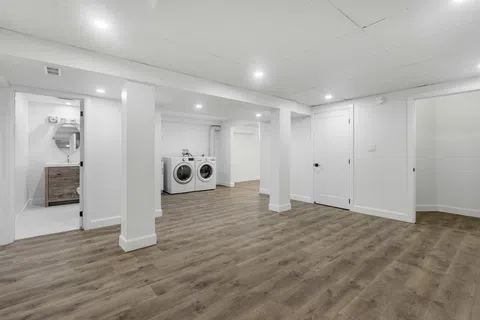 Spacious basement with wood flooring, white walls, washer and dryer, bathroom, and recessed ceiling lights.