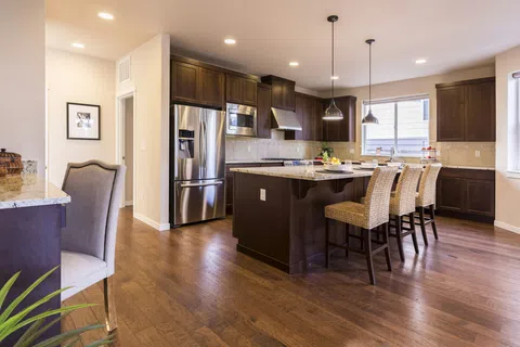 Spacious modern kitchen with dark wood cabinets, stainless steel appliances, island, and wicker bar stools under pendant lights.