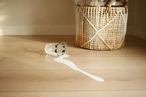 Spilled milk on wooden floor next to a woven basket with white string decoration.