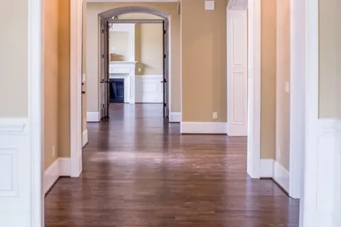 Spacious hallway with hardwood floors, beige walls, white trim, arched doorways, and chandelier lighting.