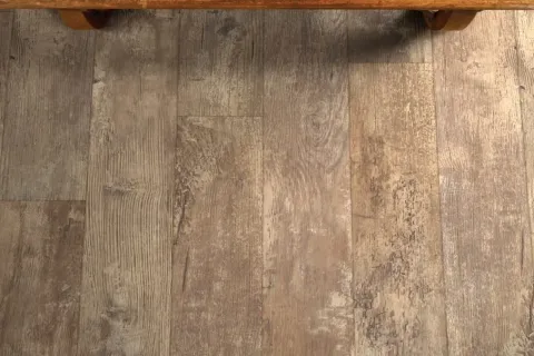 Close-up of rustic wooden floor panels with varied textures and tones beneath a wooden bench.