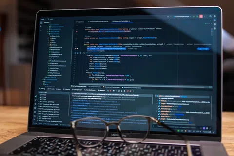 Close-up of a MacBook Pro displaying code in a programming IDE with glasses resting on the keyboard.