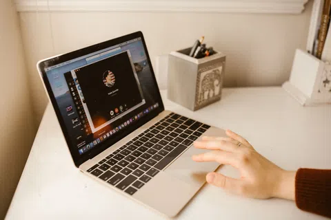 Person using a laptop on a white desk with a video call interface displayed on the screen.