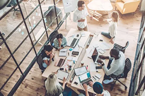 Overhead view of diverse team collaborating around a table covered with laptops, papers, and coffee in modern office