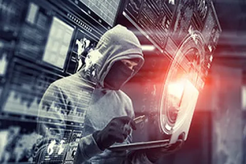 Hacker in hooded sweatshirt using laptop with digital security interface and data screens overlay