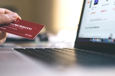 Hand holding a credit card near a laptop screen displaying an online shopping website for secure payment