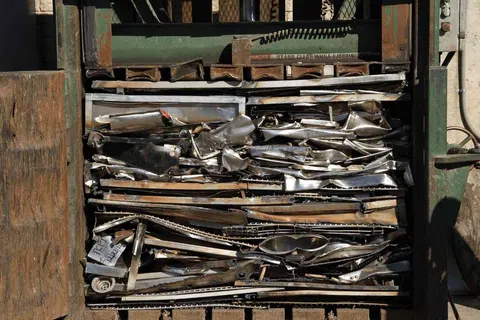 Metal scrap compacted tightly in an industrial baler machine for recycling purposes outdoors.