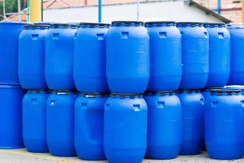 Stacked blue plastic barrels outdoors, used for storage or industrial purposes in a warehouse setting.