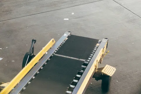Close-up of an empty yellow and black portable conveyor belt on concrete ground at an airport or warehouse.