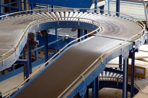 Blue industrial conveyor belts with rollers curving through a warehouse storage area with boxes