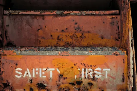 Rusty metal surface with faded white stencil text reading Safety First in an industrial setting.