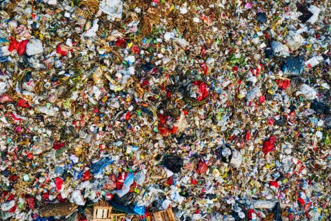 Aerial view of large landfill with scattered plastic bags, bottles, and mixed waste spread over the ground.