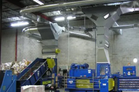 Blue industrial recycling machinery and conveyor belt in a warehouse with duct ventilation systems overhead.