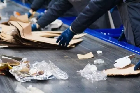 Workers sorting cardboard and plastic waste on a conveyor belt in a recycling facility