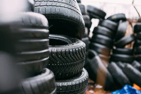 Stacked winter tires with studded treads arranged outdoors on a rainy day for storage or sale.