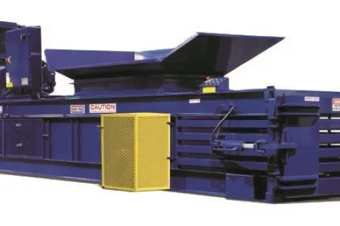 Industrial blue horizontal baler machine with yellow safety guard and open top hopper.