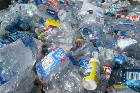 Pile of discarded plastic water bottles and containers with condensation and labels visible in daylight.