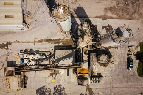 Aerial view of an industrial concrete plant with silos, machinery, and a parked black car on the right side.