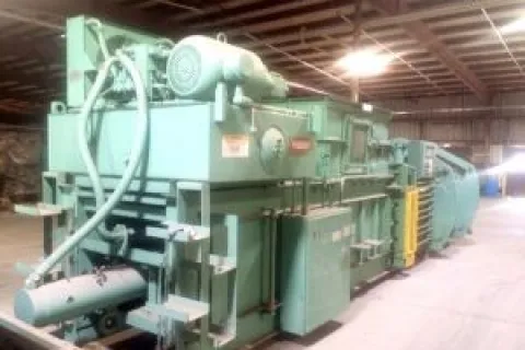 Large industrial green machine with pipes and motors inside a spacious warehouse with exposed ceiling beams.