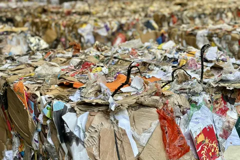 Compressed bales of mixed recyclable paper and cardboard stacked inside a recycling facility warehouse.