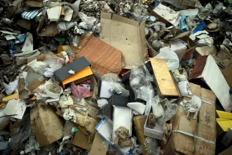 Pile of mixed waste including cardboard, paper, plastic, and packaging materials in a landfill or recycling center.
