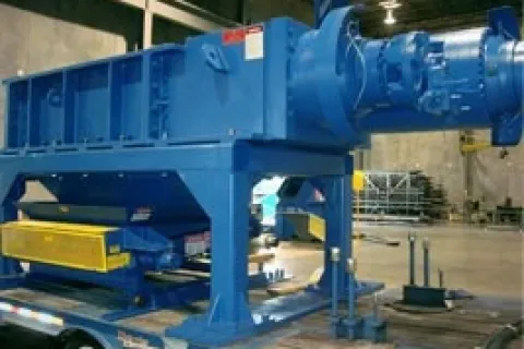 Large blue industrial machine mounted on a trailer inside a warehouse with concrete walls and equipment.