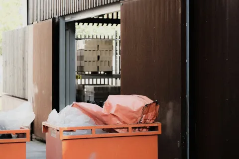 Orange industrial bins filled with plastic bags outside a modern building with wooden and metal paneling.